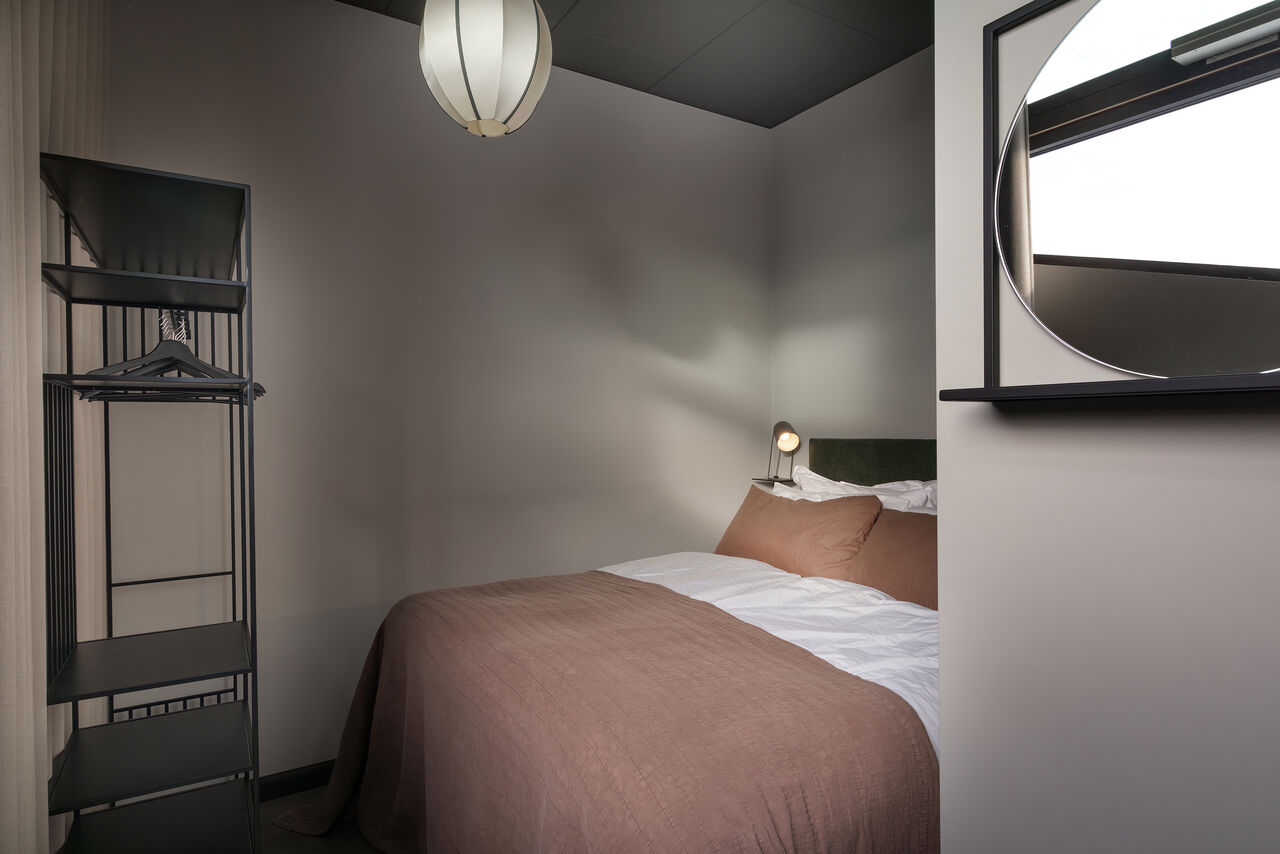 A double bed with a rust-coloured throw and a black reading lamp