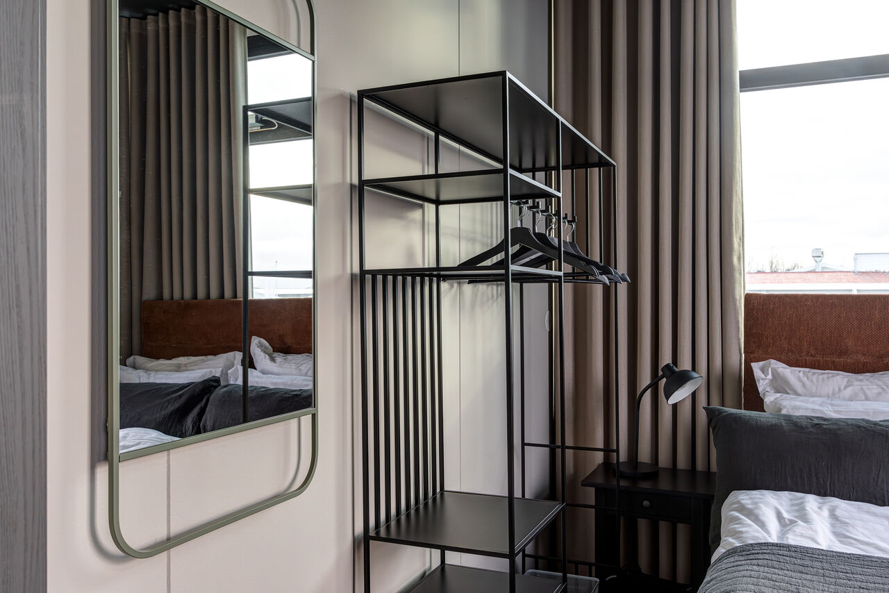 A Penthouse bedroom reflected in a tall mirror beside an open wardrobe rail