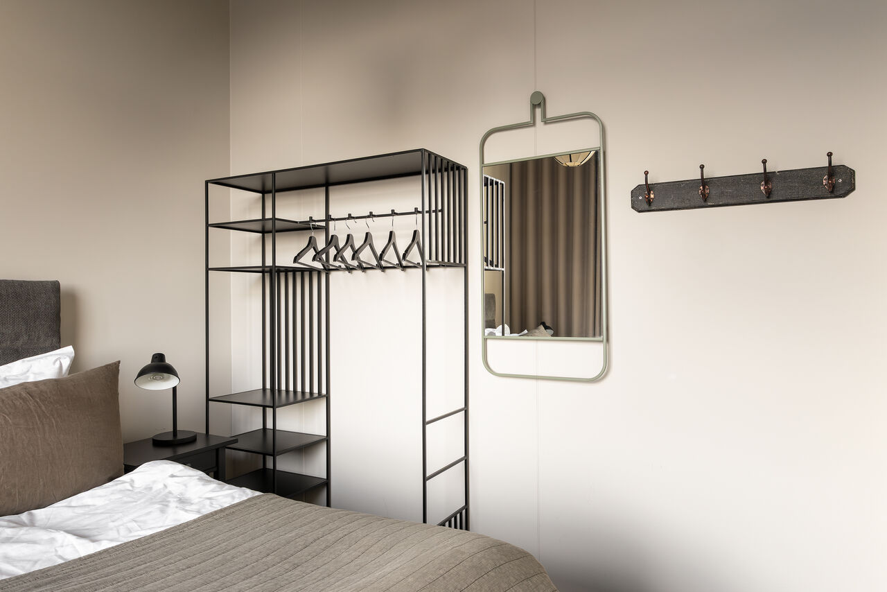 A bedroom with an open black wardrobe rail and a wall mirror