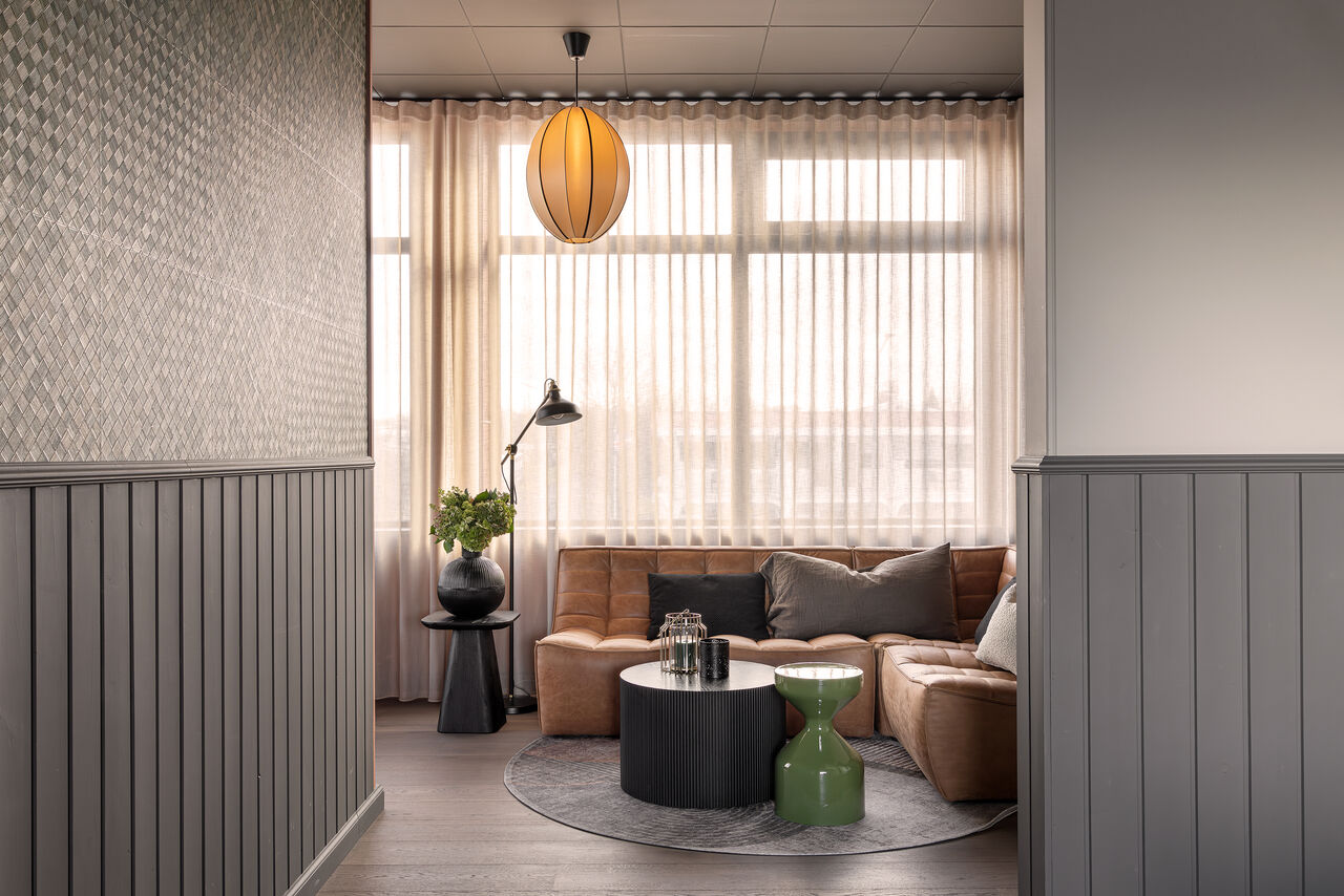 A corner lounge with a tan sofa under sheer curtains and a rattan pendant