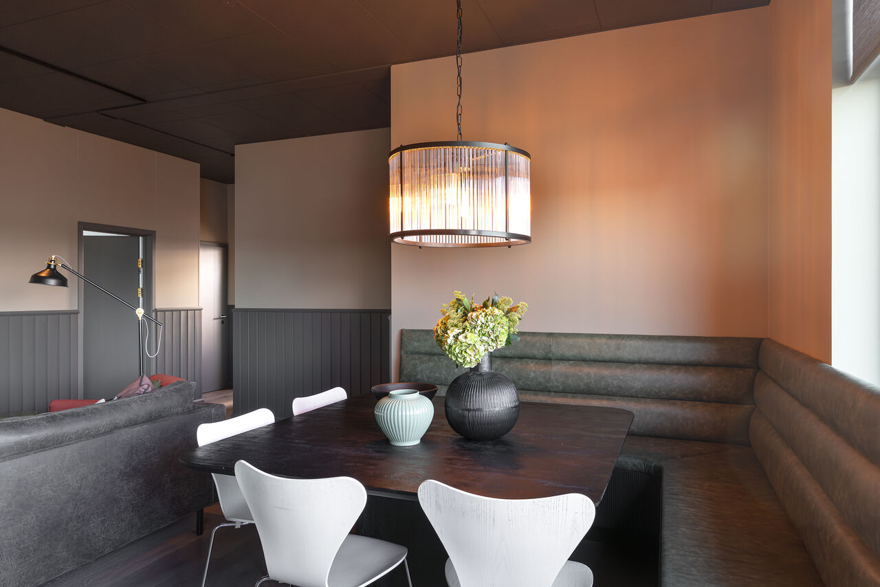 A dining nook with a banquette, white chairs and a glass pendant