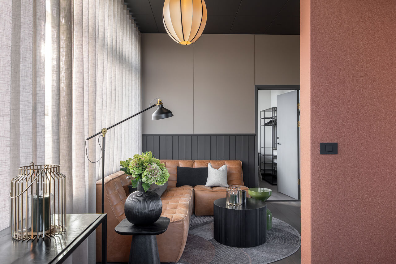 A sitting corner with a tan leather sofa beside sheer curtains