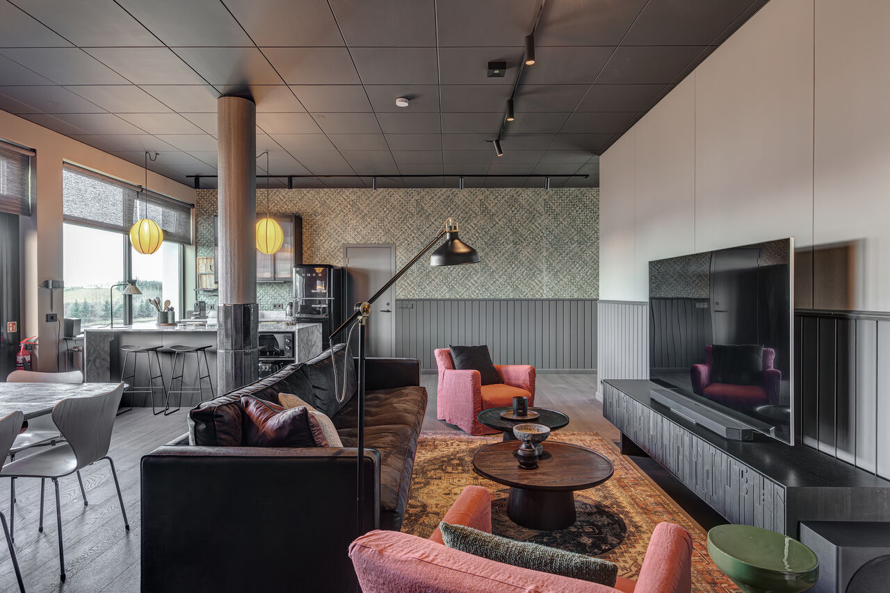 The Penthouse living room with its large screen, pink armchairs and the kitchen beyond