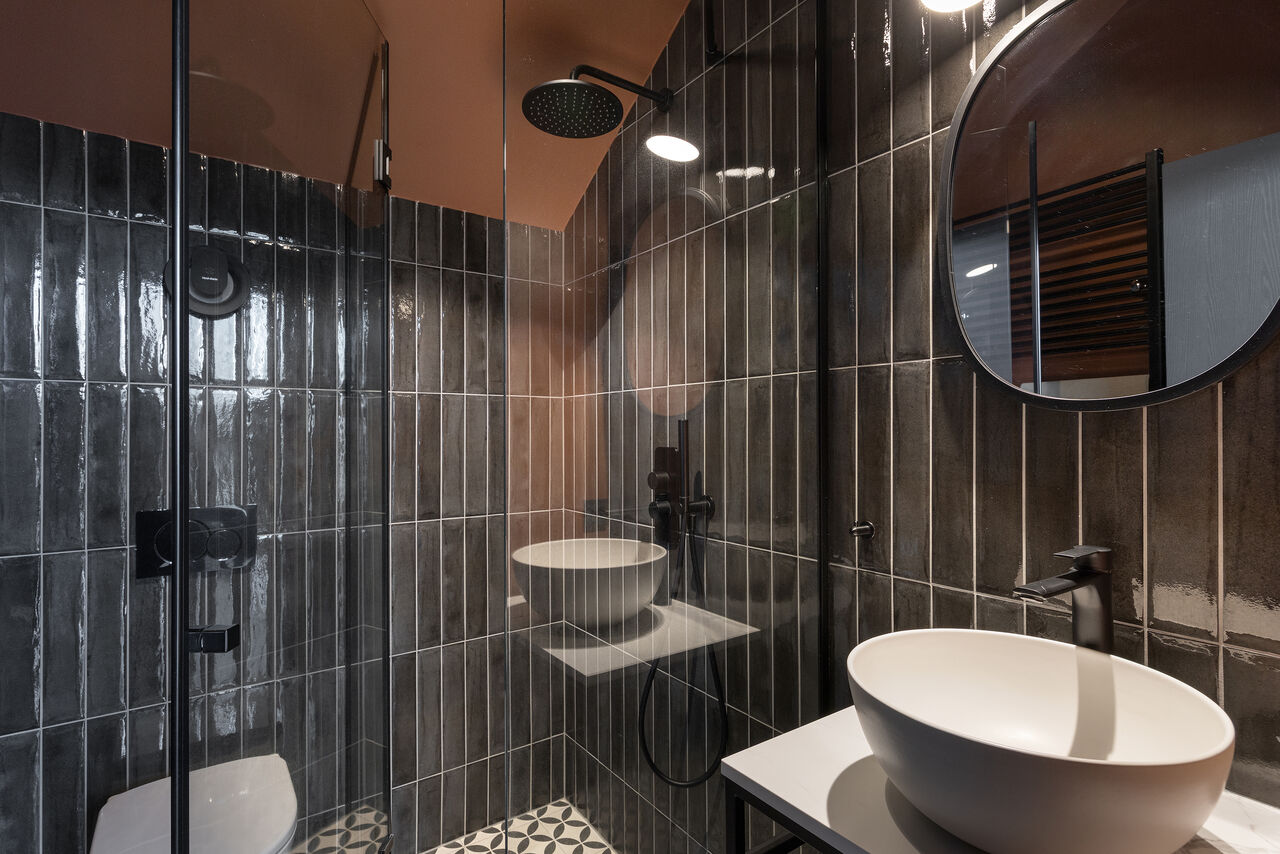 A walk-in shower in dark green tile beside a vessel sink