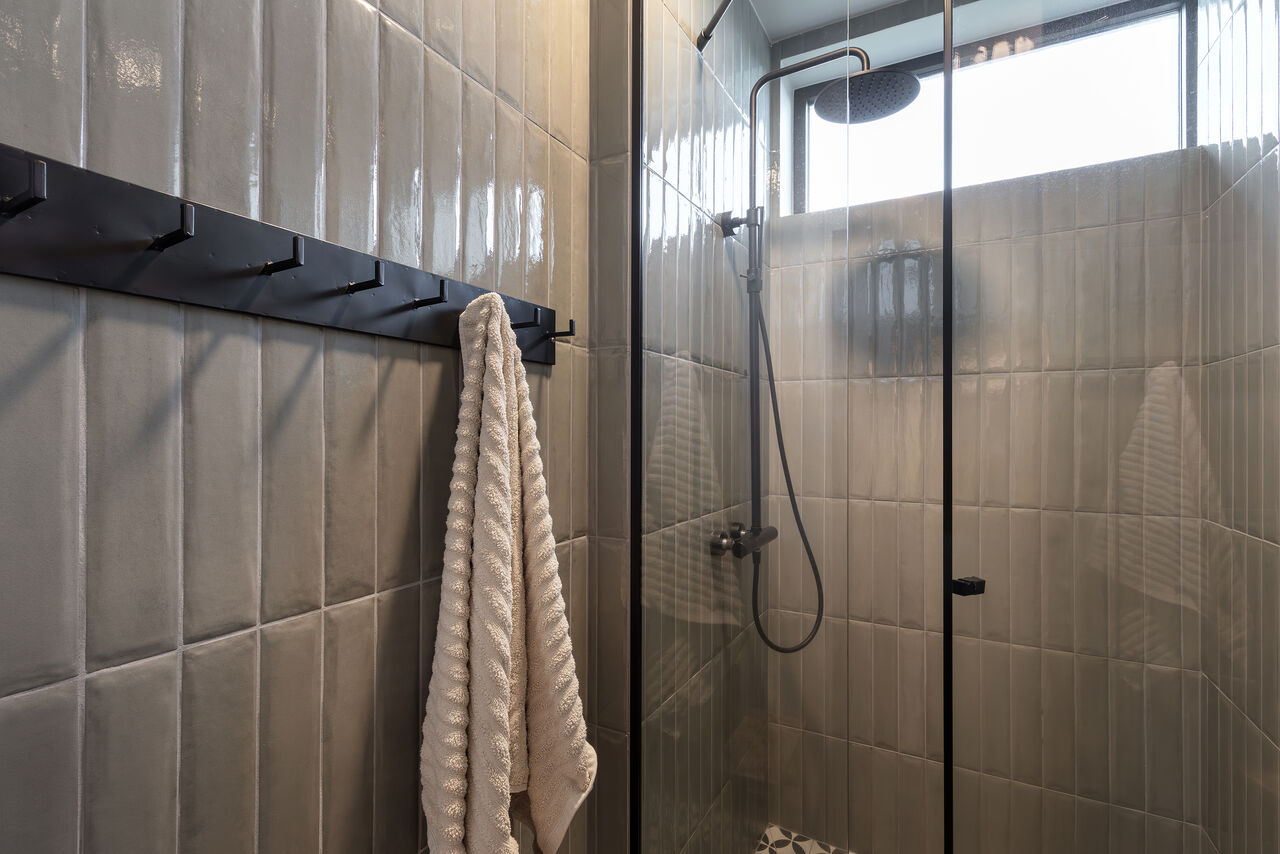 A walk-in shower in grey-green tile with a rainfall head