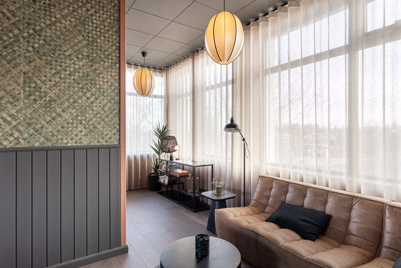 A leather sofa by tall windows beside a woven wall panel