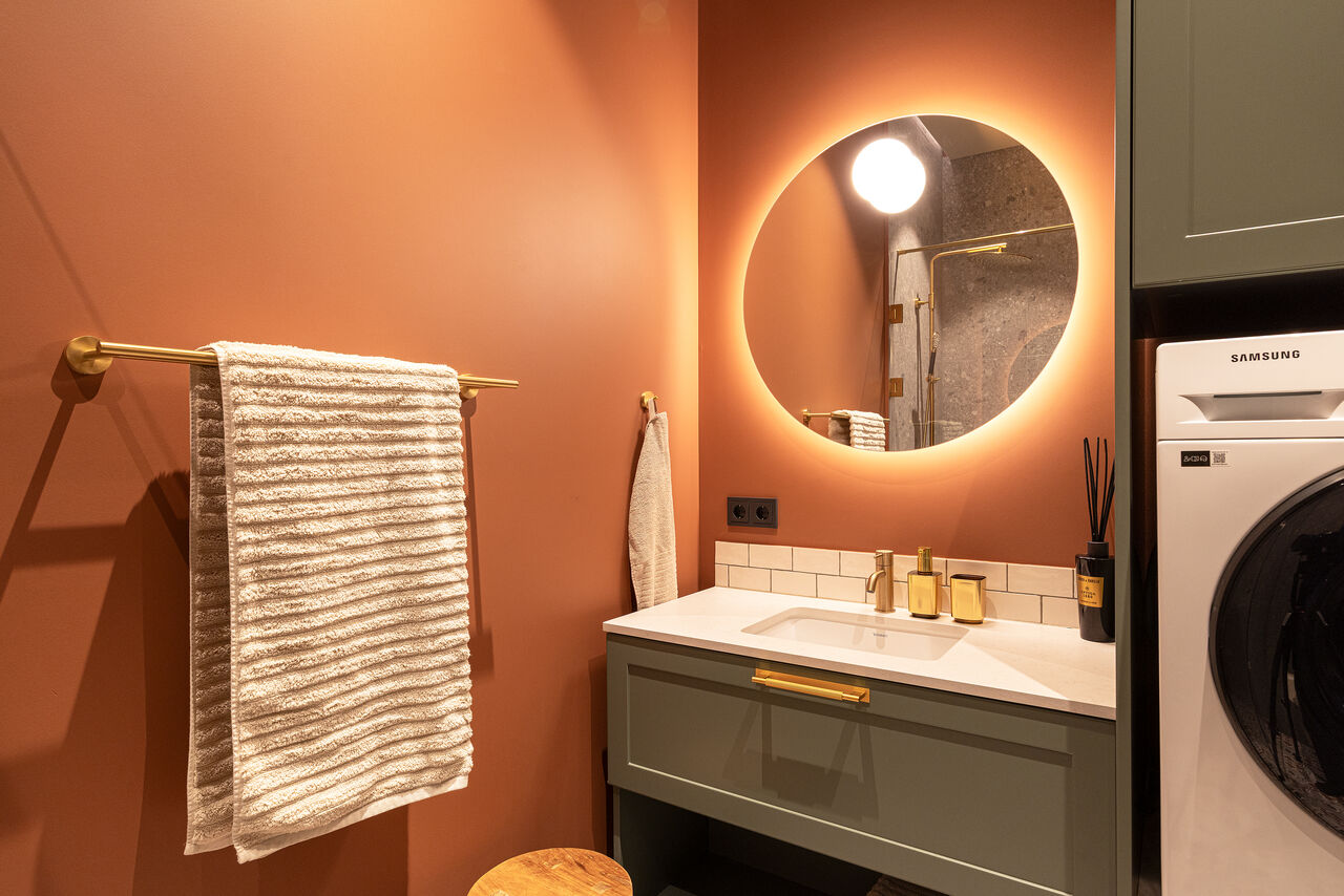 A terracotta bathroom with a backlit mirror and a washer/dryer