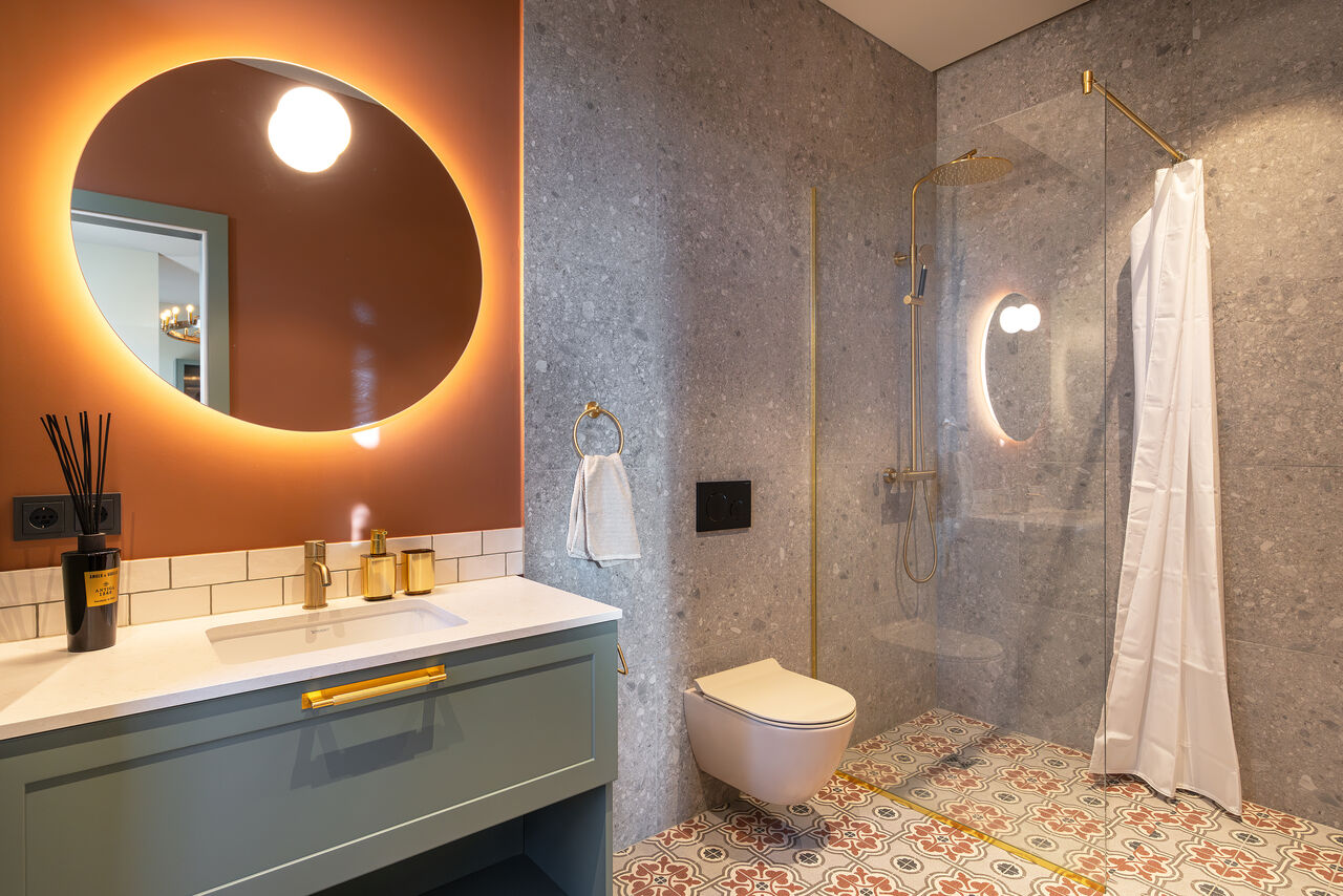 A bathroom with a backlit round mirror, stone-effect walls and a patterned floor