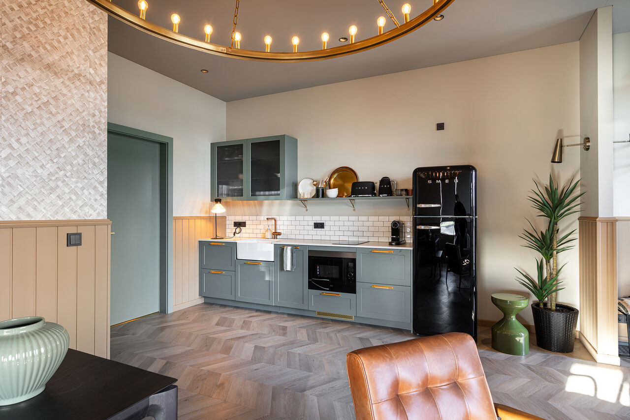 A sage-green kitchen with a black retro fridge