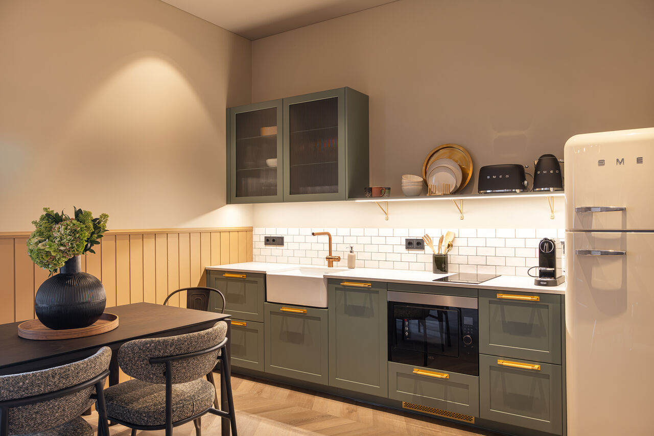 A sage-green kitchen with brass handles, a cream fridge and a dining table