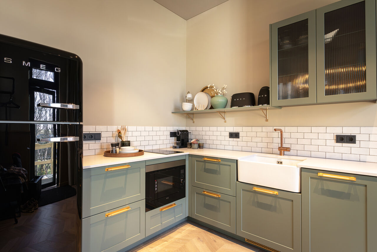 A sage-green kitchen with a black fridge, a white sink and open shelves