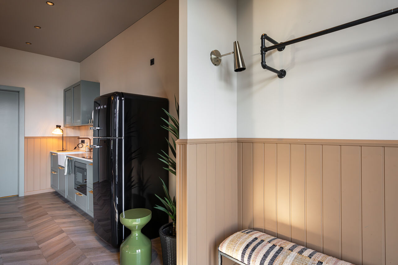 A sage-green kitchen with a black fridge beside the entrance