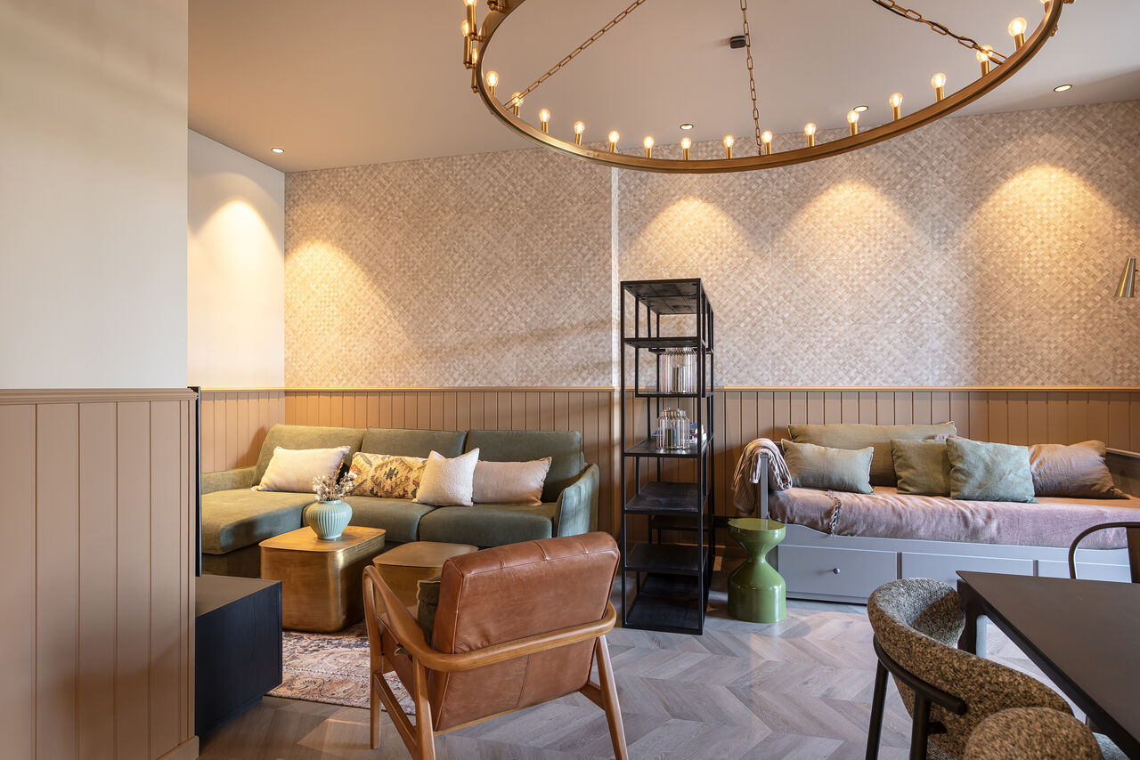 A one-bedroom apartment's lounge in sage and cream under a brass ring chandelier