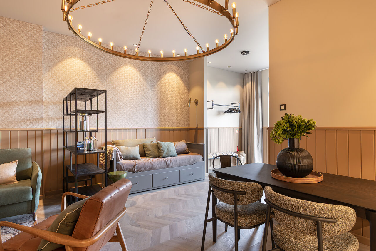 A one-bedroom living room under a brass ring chandelier, with a daybed and a dining table