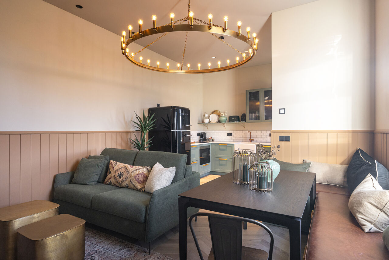 A living room with a sage sofa and dining table under a brass ring chandelier