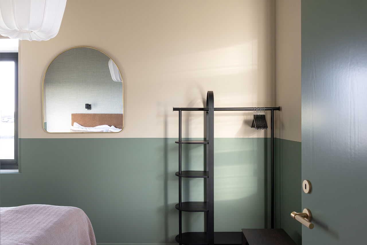 An arched mirror and open wardrobe rail in a sage and cream bedroom