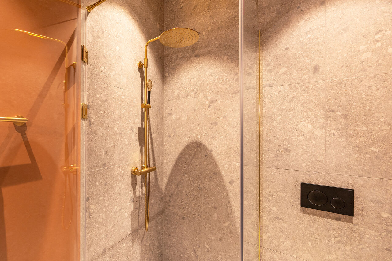 A walk-in shower with brass fittings and stone-effect tiles