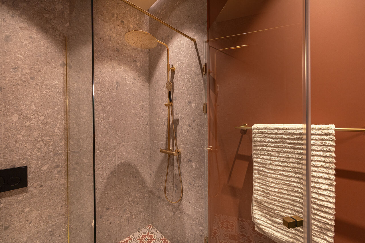 A walk-in shower with brass fittings behind a glass screen